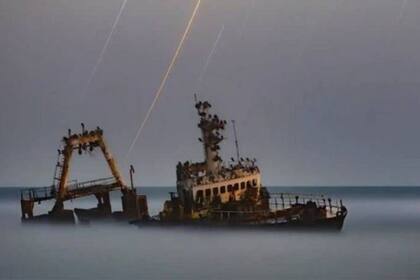Un barco parece surcar la niebla, iluminado por estelas de estrellas que brillan a través del cielo nublado