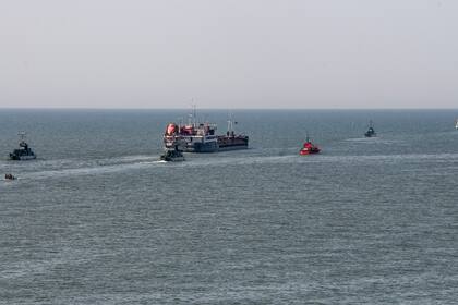 Un barco ruso, al centro, escoltado por botes militares rusos, sale del puerto de Mariúpol, en territorio controlado por la República Popular de Donetsk, en el este de Ucrania, el martes 31 de mayo de 2022. (AP Foto)