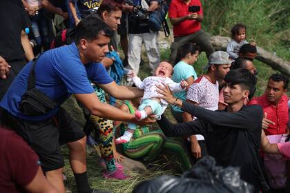 Un bebé se pasa de una persona a otra mientras los migrantes se dirigen al Río Grande para cruzar para ingresar a los Estados Unidos el 11 de mayo de 2023 en Matamoros, México