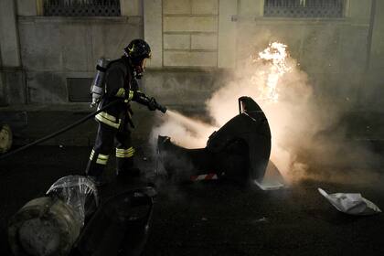 Un bombero italiano apaga un contenedor de basura en llamas durante una protesta de activistas de extrema derecha contra las medidas de restricción del gobierno para frenar la propagación del coronavirus, en el centro de Turín, el 26 de octubre de 2020