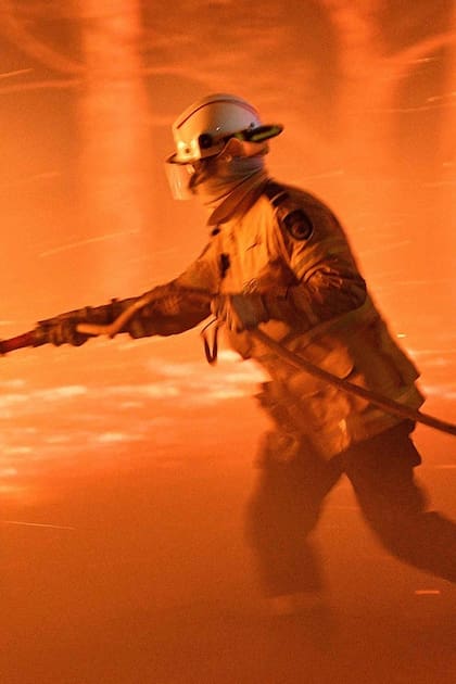 Un bombero lucha contra el fuego y las brasas en un esfuerzo por proteger las casas cercanas de los incendios forestales cerca de la ciudad de Nowra, el 31 de diciembre. Australia movilizó barcos y aviones militares para ayudar a las comunidades arrasadas por los apocalípticos incendios.