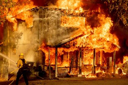 Un bombero rocía agua en un intento por impedir que un incendio se propague a residencias vecinas el sábado 10 de julio de 2021, en Doyle, California. (AP Foto/Noah Berger)