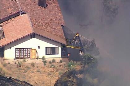 Un bombero rocía agua mientras varias casas se queman durante un incendio forestal en una comunidad ubicada en una ladera, en California, el lunes 5 de agosto 2024, en el condado de San Bernardino. (ABC7 Los Angeles vía AP)