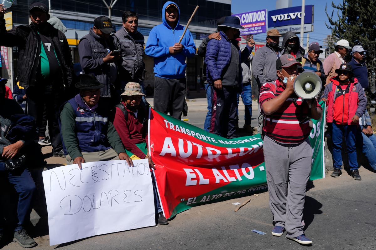 Un camionero grita consignas por un megáfono mientras otro sostiene un cartel que dice "Necesitamos dólares" mientras bloquean la carretera de El Alto a Oruro para protestar por la escasez de dólares estadounidenses y combustible en El Alto, Bolivia. (AP Foto/Juan Karita)