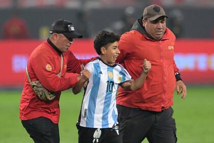 Un chico con la camiseta argentina es sacado de la cancha por personal de seguridad luego de haber invadido el terreno de juego; se llevó una foto con Messi