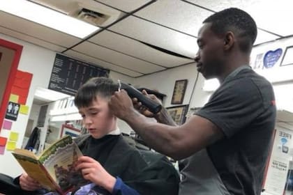Un chico lee mientras recibe un corte de pelo