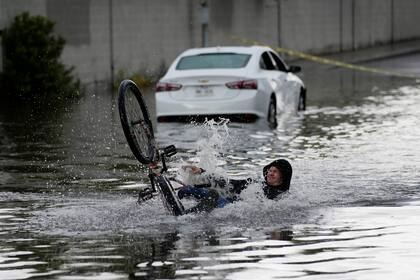 Un ciclista cae mientras intenta atravesar una calle inundada, cerca de un automóvil varado, el viernes 1 de septiembre de 2023, en Las Vegas. (Foto AP/John Locher)