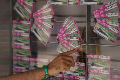 Un cliente señala un boleto de lotería que quiere comprar en la Ciudad de México, el lunes 13 de septiembre de 2021. La lotería de México está regalando como premios propiedades incautadas a los narcotraficantes, entre ellas una casa que perteneció a Joaquín "El Chapo" Guzmán. (AP Foto/Fernando Llano)