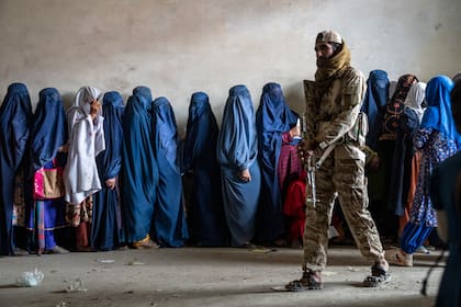Un combatiente del Talibán monta guardia mientras mujeres esperan a recibir raciones de comida distribuidas por un grupo humanitario, el 23 de mayo de 2023, en Kabul. (AP Foto/Ebrahim Noroozi, Archivo)