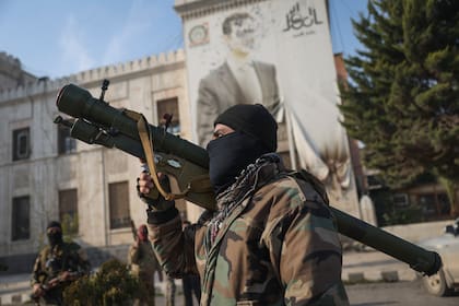 Un combatiente sirio de oposición sostiene un lanzacohetes frente a la oficina del gobierno regional, en cuya fachada se muestra una imagen del presidente sirio, Bashar Assad, rodeada de disparos, tras la toma de la ciudad de Hama por parte de la oposición, en Siria, el viernes 6 de diciembre de 2024. (AP Foto/Ghaith Alsayed)