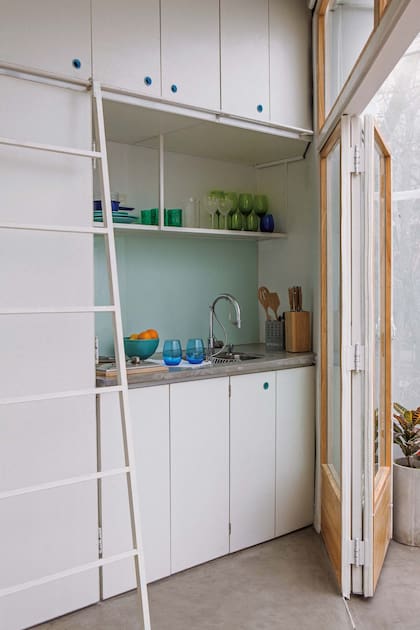 Un detalle vistoso y sustentable, todas las puertas tienen tiradores turquesas, de plástico reciclado de Proyecto Mutan. La fina escalera, que corre sobre una guía incorporada en el mueble, permite aprovechar el lugar de guardado en altura.