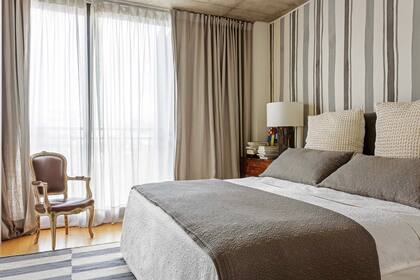 Un doble cortinado –voile translúcido detrás y lino por delante– y un género pintado a mano en la pared de la cabecera marcan el cálido tono del cuarto principal.