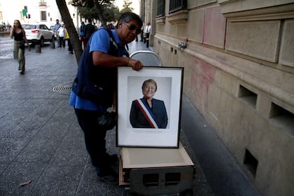 Un empleado retira de un edificio público el retrato de Bachelet, en Santiago