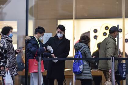 Un empleado revisa la temperatura corporal de visitantes a una tienda de Apple en Shanghai