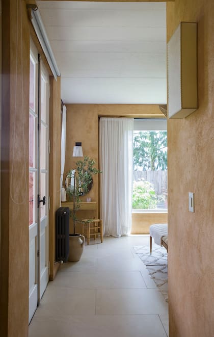 Un espacio que conecta con la naturaleza: paredes en tonos tierra, luz natural filtrada por cortinas livianas y detalles orgánicos como la planta y el espejo redondo crean un ambiente cálido y relajado.