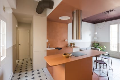 Un extractor cilíndrico en acero brillante (Electrolux) baja sobre el anafe. Otro círculo simétrico en la zona de trabajo aloja una luz creando el efecto de una lámpara de techo sin agregar elementos.