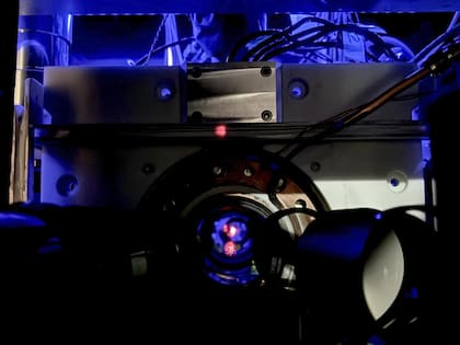 Un gas extremadamente frío de átomos de estroncio está atrapado en una red de luz conocida como red óptica. Los átomos se mantienen en un ambiente de vacío ultra alto, lo que significa que casi no hay aire ni otros gases presentes. Este vacío ayuda a preservar los delicados estados cuánticos de los átomos, que son frágiles. El punto rojo que ves en la imagen es un reflejo de la luz láser utilizada para crear la trampa atómica.