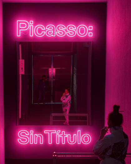 Un gran espejo con el nombre de la exposición escrito en letras de neón fucsia es lo primero que ve el espectador al ingresar a la antesala