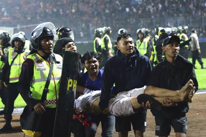Un grupo de aficionados carga a un hombre herido en los enfrentamientos durante un partido de fútbol en Malang, Indonesia, el sábado 1 de octubre de 2022 (AP Foto/Yudha Prabowo)