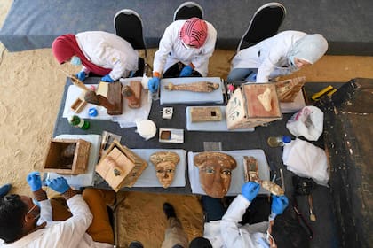 Un grupo de arqueólogos limpian e inspeccionan las máscaras funerarias encontradas junto a los sarcófagos