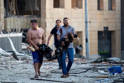 Un grupo de hombres heridos trasladan una mujer. La explosión tuvo lugar en la zona portuaria de Beirut