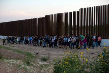 Un grupo de migrantes junto a un tramo del muro fronterizo mientras esperan a ser recogidos por la Patrulla Fronteriza, el sábado 21 de mayo de 2022, en Eagle Pass, Texas.  (AP Foto/Dario Lopez-Mills)