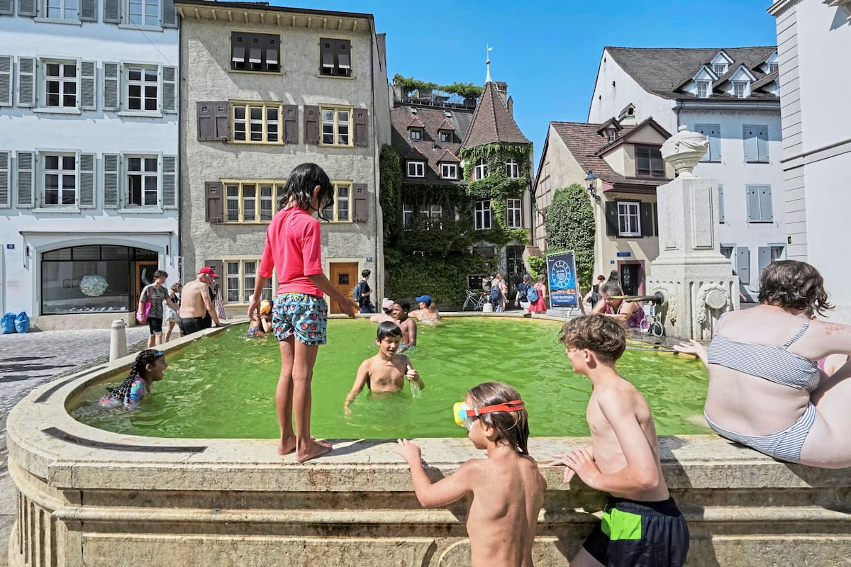 Un grupo de niños se baña en una fuente durante una ola de calor en el centro de Basilea, Suiza, el lunes 30 de junio de 2025