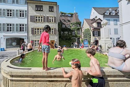 Un grupo de niños se baña en una fuente durante una ola de calor en el centro de Basilea, Suiza, el lunes 30 de junio de 2025