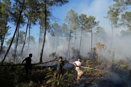 Un grupo de personas sostiene una manguera e intenta extinguir un fuego cerca de Lacanau, mientras los incendios arden a las afueras de Burdeos, Francia