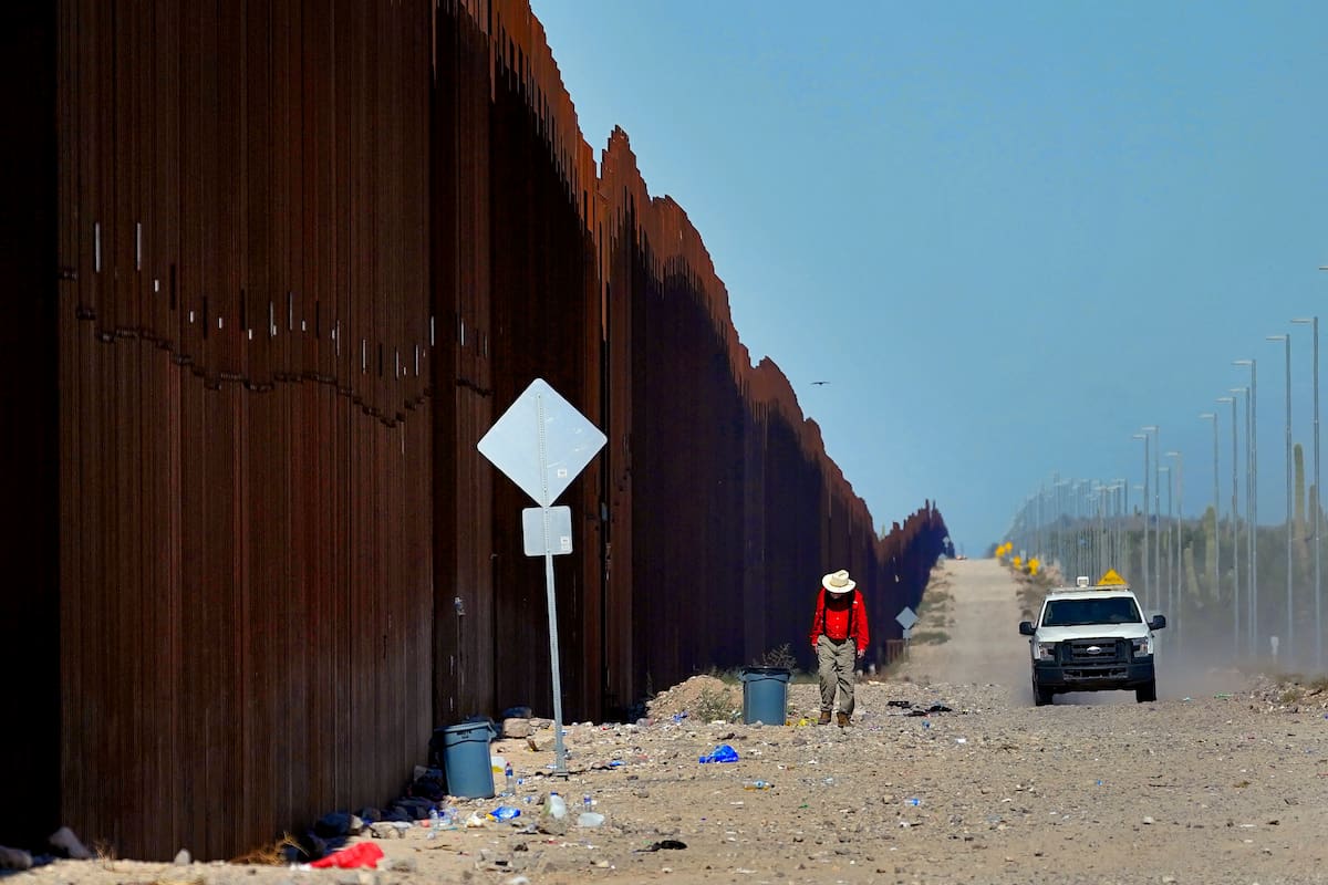 Un hombre camina a lo largo del muro fronterizo al tiempo que un agente de la Patrulla Fronteriza de Estados Unidos patrulla el área, cerca de Lukeville, Arizona. (AP Foto/Matt York)
