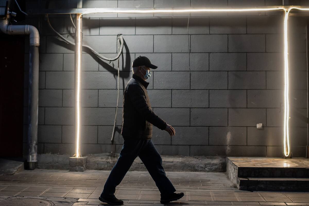 Un hombre camina con barbijo en una calle solitaria de Pekín