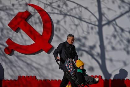 Un hombre camina con un niño pequeño junto a un logotipo del Partido Comunista expuesto cerca de una zona residencial en Pekín, el jueves 2 de marzo de 2023