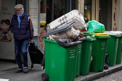 Un hombre camina frente a botes de basura sin recolectar, el jueves 9 de marzo de 2023, en París. (AP Foto/Michel Euler)