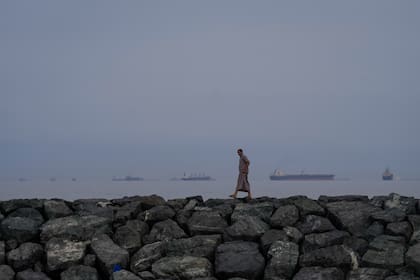 Un hombre camina por la orilla del mar mientras buques petroleros y de carga se alinean en el estrecho de Ormuz, vistos desde Khor Fakkan, Emiratos Árabes Unidos
