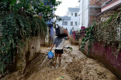 Un hombre camina por un callejón embarrado con pertenencias sacadas de su casa en Katmandú, Nepal, el lunes 30 de septiembre de 2024, tras una inundación causada por fuertes lluvias. (AP Foto/Gopen Rai)
