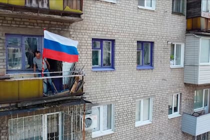 Un hombre coloca una bandera rusa en el balcón de un edificio en Lysychansk, que el fin de semana cayó en manos del Kremlin y los separatistas