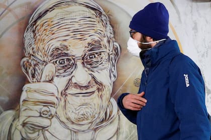 Un hombre con barbijo camina al lado de un mural del Papa Francisco en el metro de Roma