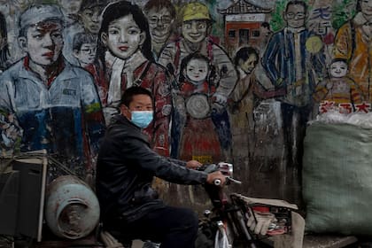 Un hombre con barbijo en medio de las preocupaciones por el coronavirus conduce su moto por una calle en Wuhan