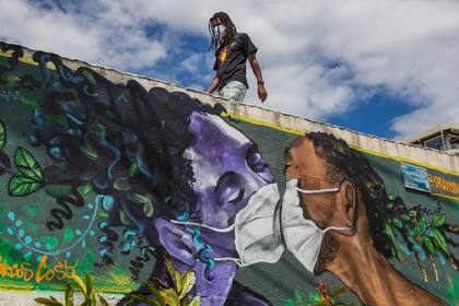 Un hombre con barbijo pasa junto a un graffiti del artista Marcos Costa, en la entrada de la favela Solar de Unhao en Salvador el 15 de abril de 2020, en medio de la pandemia de coronavirus