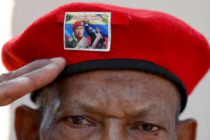 Un hombre con la emblemática boina roja del difunto presidente de Venezuela Hugo Chávez, adornada con una foto del actual presidente Nicolás Maduro con Chávez, saluda mientras espera para visitar los restos del líder en el sexto aniversario de su muerte, en esta fotografía de archivo del 5 de marzo de 2019, en Caracas. (AP Foto/Eduardo Verdugo)