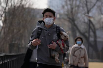 Un hombre con mascarilla lleva en brazos a un perro con suéter, el domingo 20 de marzo de 2022 en Beijing. (AP Foto/Ng Han Guan)