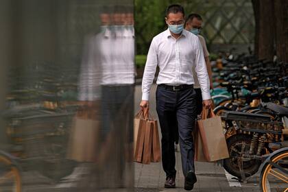Un hombre, con mascarilla para protegerse del coronavirus, camina cargado con bolsas por una vereda en Beijing, el 13 de septiembre de 2021. (AP Foto/Andy Wong)