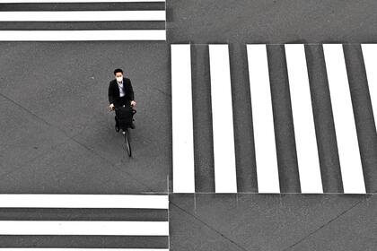 Un hombre con una máscara facial en medio de las preocupaciones por el coronavirus cruza una calle en bicicleta en Tokio el 25 de mayo de 2020
