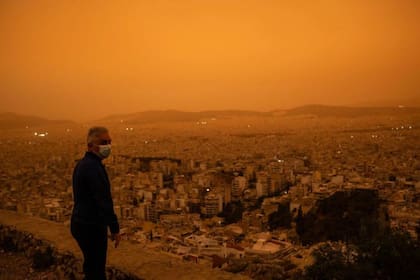 Un hombre con una mascarilla mira hacia la ciudad de Atenas desde la colina Tourkovounia