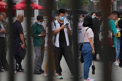 Un hombre consulta su celular mientras hace fila con otras personas para recibir la vacuna contra el Covid-19 en Pekín