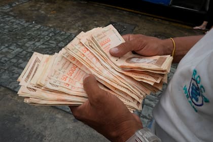Un hombre cuenta bolívares por el valor de un dólar en una parada de autobús en Caracas (AP Photo/Ariana Cubillos,File)