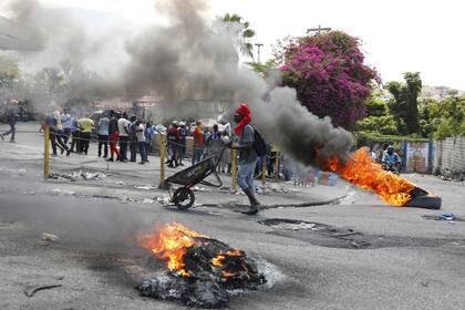 Un hombre empuja una carretilla frente a neumáticos en llamas durante una protesta para exigir la renuncia del primer ministro, Ariel Henry, el 7 de marzo, en Puerto Príncipe