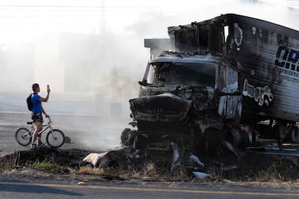 Un hombre en bicicleta toma una fotografía de un camión calcinado en una carretera cerca de Acatlán de Juárez, estado de Jalisco