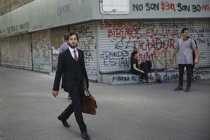 Un hombre en traje de negocios camina cerca de un grupo de estudiantes después de las protestas contra el Gobierno en Santiago