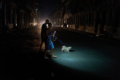 Un hombre enciende una linterna mientras cruza una calle con su perro durante un apagón en La Habana, el miércoles 10 de septiembre de 2025